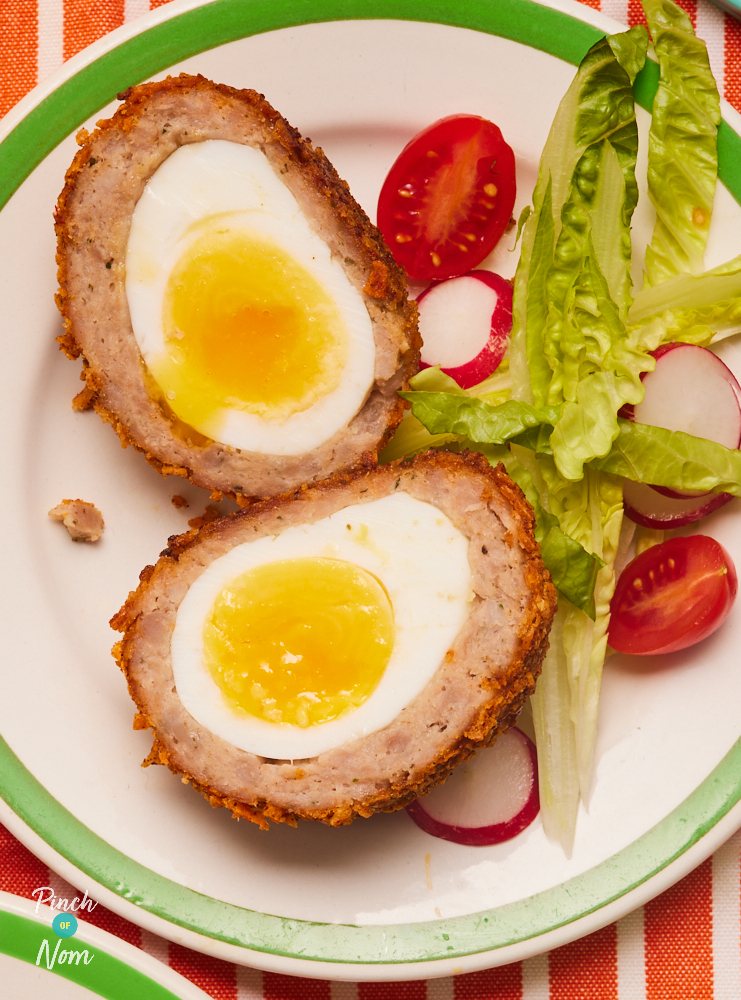 A close-up shows one of Pinch of Nom's Zinger Scotch Eggs, served with a side salad. The scotch egg has been cut in half, revealing the cross section of layers of freshly-boiled egg, sausage and crispy Zinger coating.