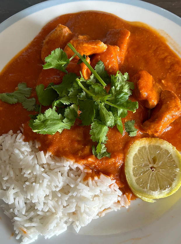 Pinch of Nom's Air Fryer Chicken Tikka Masala (from the Air Fryer cookbook) is plated up alongside a fluffy portion of rice, with a garnish of fresh coriander leaves and a lemon wedge.