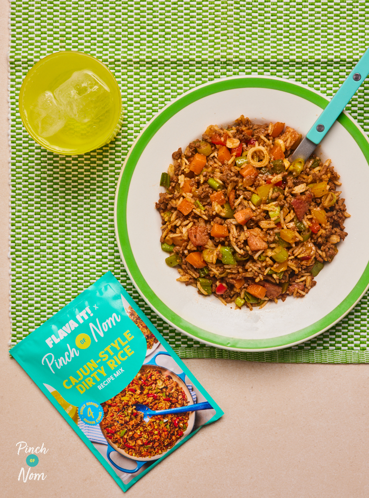 Flava It! X Pinch of Nom's Cajun-Style Dirty Rice is served on a white plate with a bright green rim. The plate is set on a green place mat, next to a sachet of the recipe mix and water in a bright yellow glass.