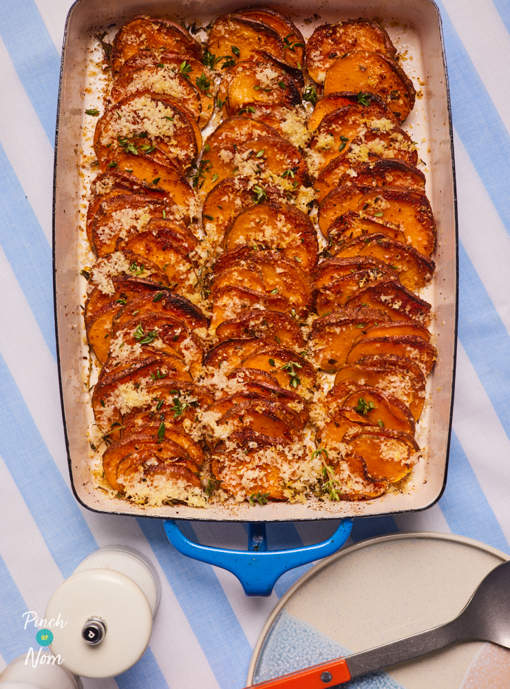 Pinch of Nom's Garlic and Parmesan Sweet Potatoes are served in a rectangular oven dish, set on a pale blue and white striped tablecloth. The potatoes are golden brown and crispy at the edges, with melted cheese all over the top.