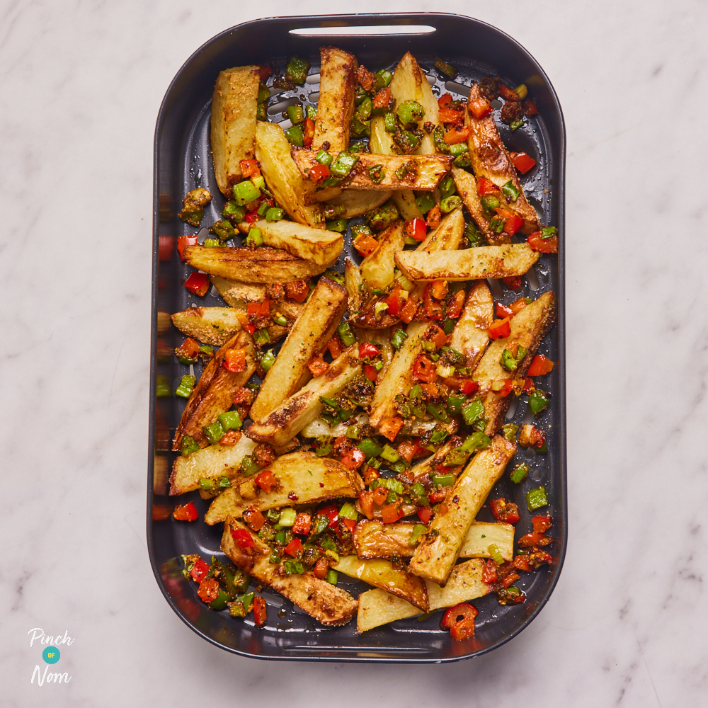 Pinch of Nom's Flava It! Salt and Pepper Chips are fresh from the air fryer, still in the air fryer basket. The chips are crunchy and golden, with peppers and spring onions mixed in.