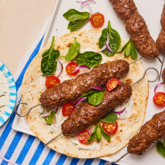 Pinch of Nom's Flava It! Burger and Kebab recipe mix has been used to make Seekh Kebabs. The kebabs are served on a flatbread, with lettuce leaves and cherry tomatoes.