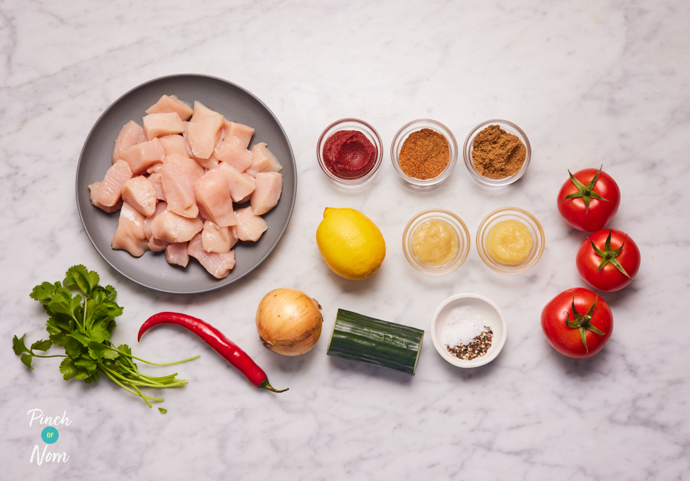 The ingredients for Pinch of Nom's slimming-friendly Zesty and Tangy Chaat-Style Chicken are laid out on a kitchen surface. Each ingredient is measured out, ready to begin cooking.