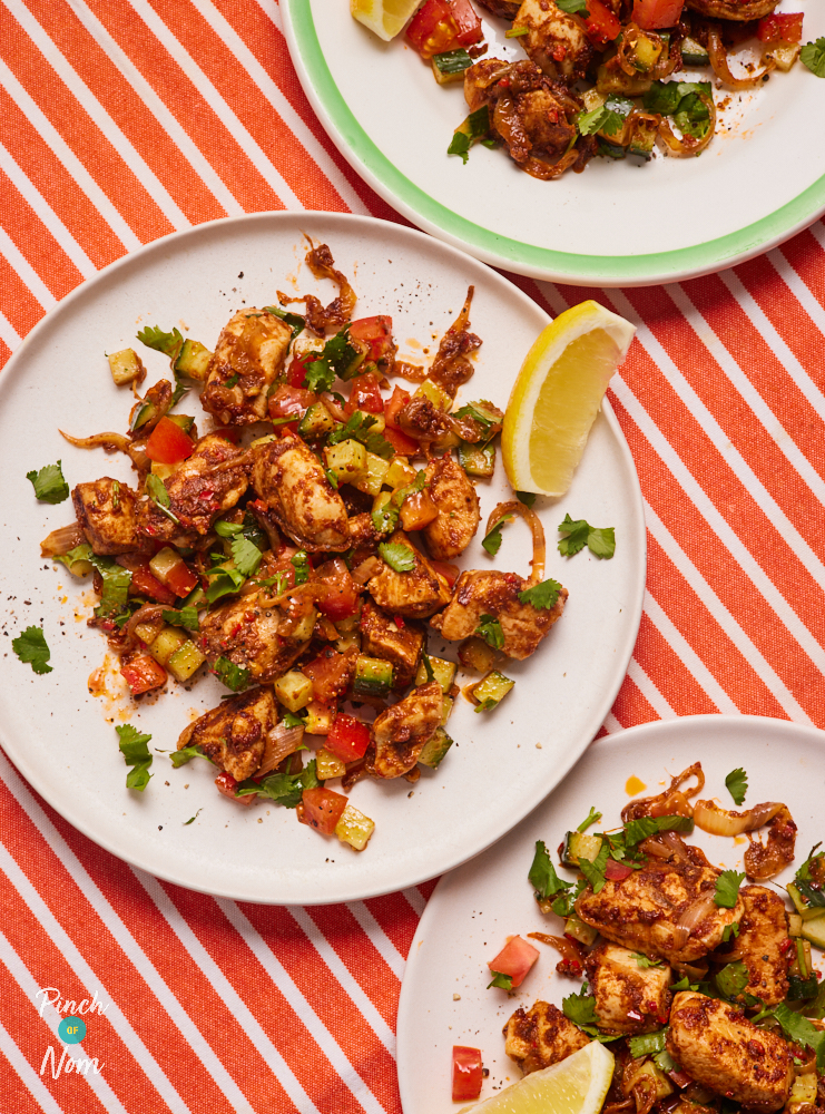 A close-up of a table set with Pinch of Nom's Zesty and Tangy Chaat-Style Chicken recipe. It's garnished with a lemon wedge, waiting to be squeezed on top.