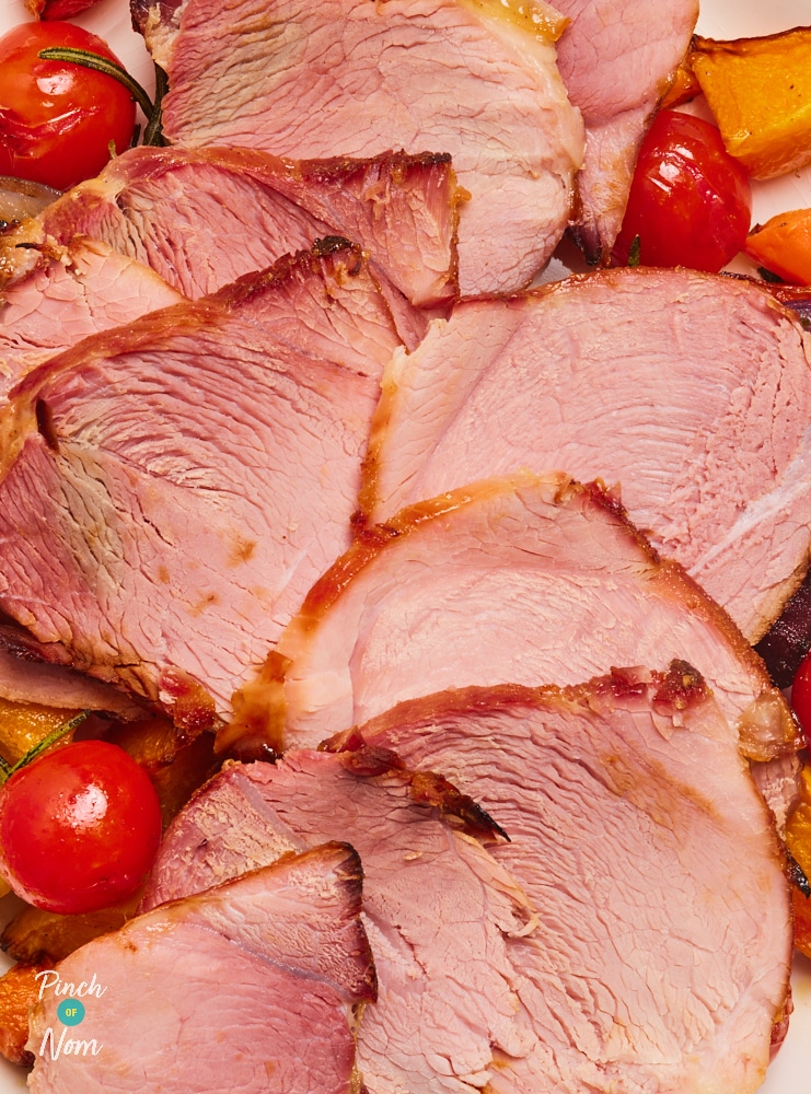 Pinch of Nom's Honey-Glazed Ham is served, sliced evenly and presented on a bed of browned, oven-roasted root vegetables.