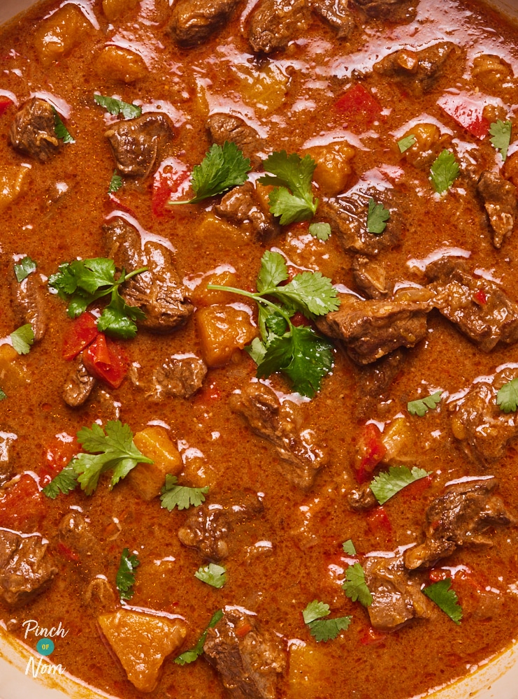 A close-up of Pinch of Nom's Beef and Butternut Squash Curry where you can see that the sauce is rich and thick, with butternut squash and beef chunks poking through. Fresh coriander is leaves are scattered on top.