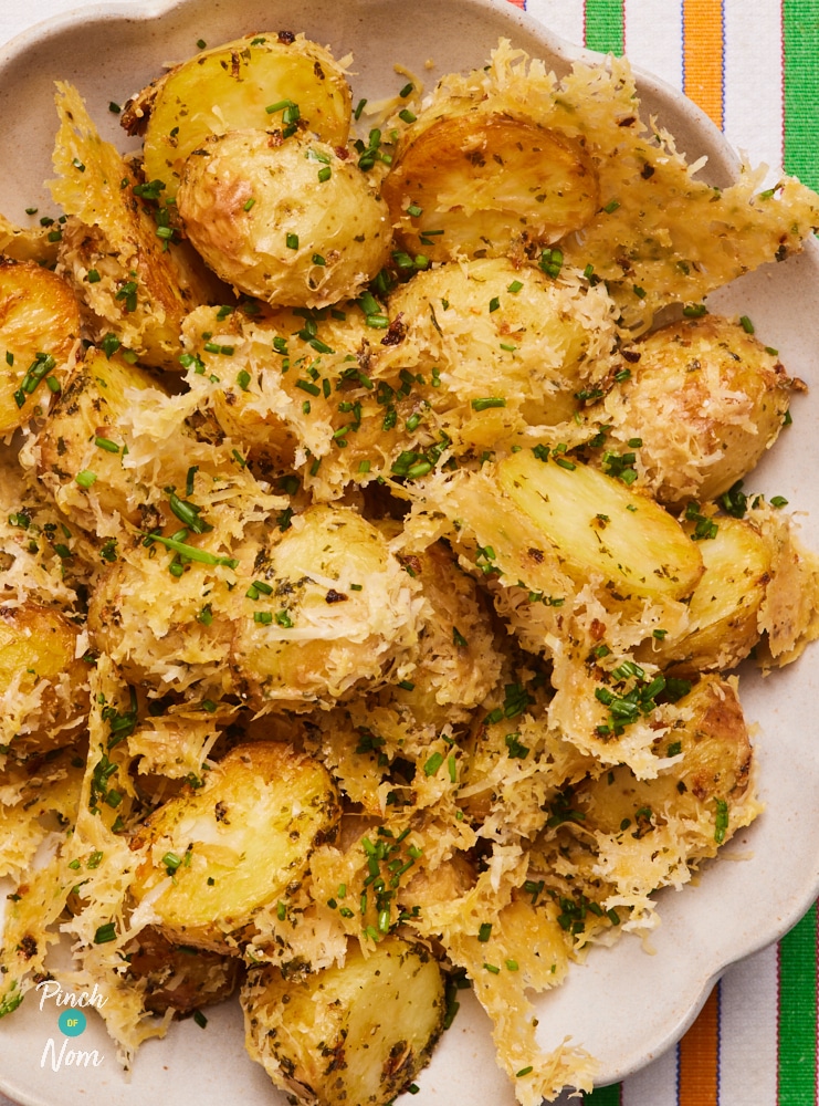 A close-up shows Pinch of Nom's Parmesan Potatoes, ready to be served. They are golden brown with a crispy cheese crust, garnished with chopped fresh chives.