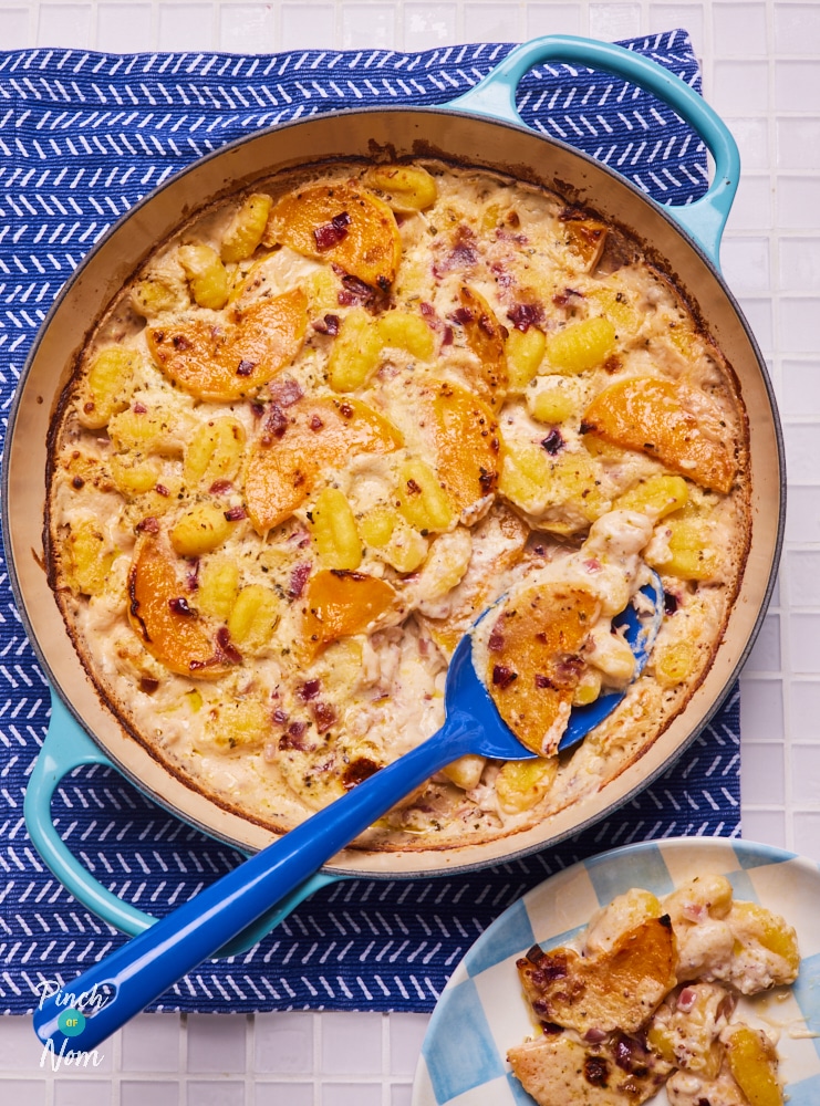 Pinch of Nom's Butternut Squash and Sage Gnocchi is served in a blue casserole dish, resting on a deeper blue tea towel. A blue serving spoon rests in the dish, and a portion has been scooped out and served on a plate set nearby.