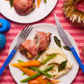 A colourful, festive table is set with two portions of Pinch of Nom's slimming-friendly Christmas Chicken Thighs recipe; the chicken thigh on the closest plate is cut open, to reveal the sausage stuffing inside. It's served with mashed potatoes and steamed veg.