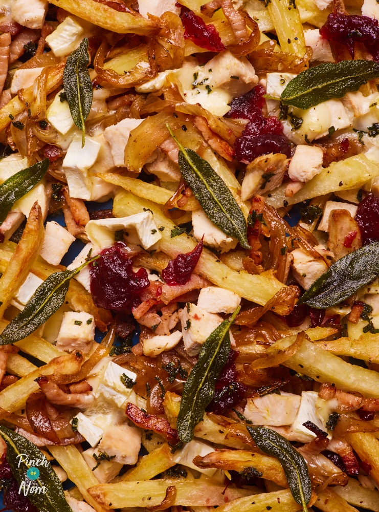 A close-up of Pinch of Nom's Christmas Loaded Fries. The golden fries are topped with turkey, bacon, melted brie, cranberry sauce and fresh sage.