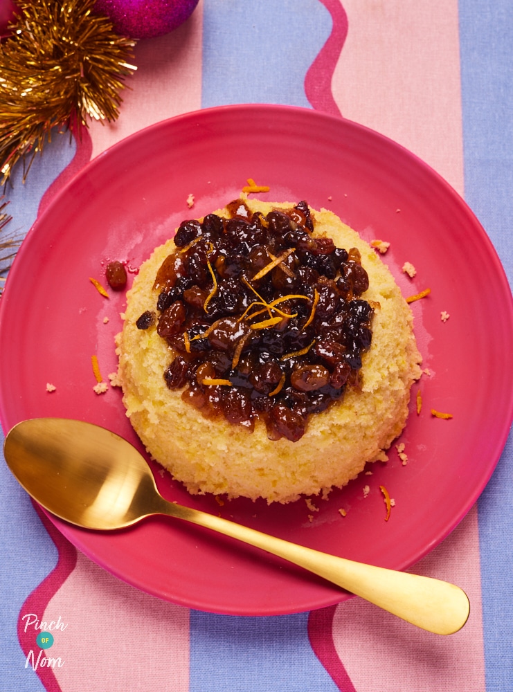 Pinch of Nom's Mince Pie Pudding is served on a red plate. The moist orange sponge is topped with a juicy layer of mincemeat. A gold spoon rests on the plate, ready to dig in.