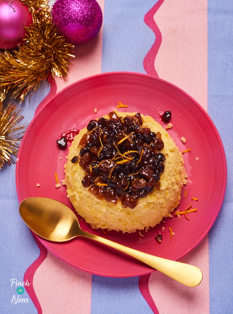 Pinch of Nom's Mince Pie Pudding is served on a red plate. The moist orange sponge is topped with a juicy layer of mincemeat. A gold spoon rests on the plate, ready to dig in.