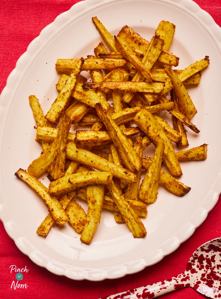 A large, freshly-baked batch of Pinch of Nom's Spiced Parsnip Fries recipe on a large serving plate, served on a table laid with a Christmassy bright-red tablecloth.