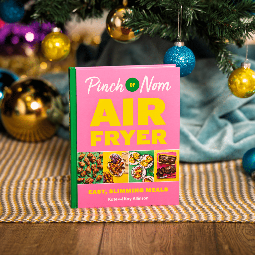 A copy of Pinch of Nom: Air Fryer stands under a colourfully decorated Christmas tree, as though it has just been unwrapped on Christmas morning.