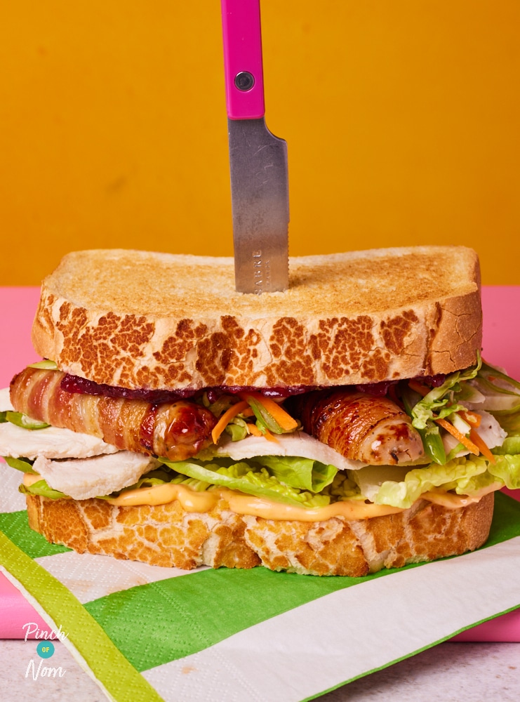 Pinch of Nom's slimming-friendly Boxing Day sandwich is served on a colourful countertop against a bright yellow backdrop, with a butter knife standing upright in the sandwich to show its sturdiness.