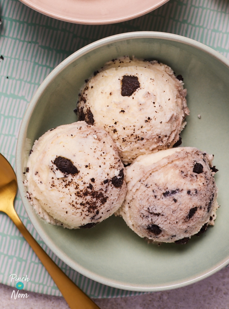 In a pale green bowl, three scoops of Pinch of Nom's slimming-friendly Ninja Creami Cookies and Cream Ice Cream is served with a gold-plated spoon ready to dig in.