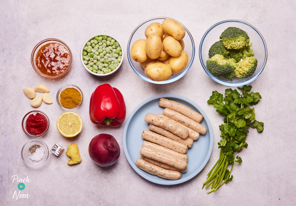 The ingredients for Pinch of Nom's Curried Sausage Traybake are laid out on a kitchen counter, ready to begin cooking.