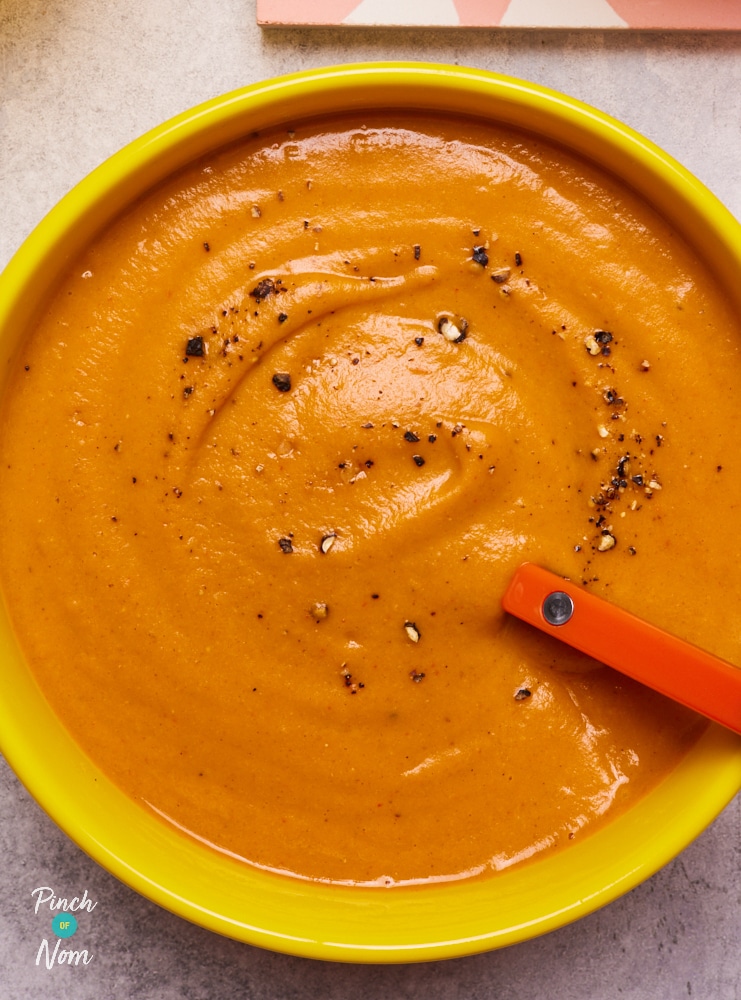 A bowl is filled with an eye-catching portion of Pinch of Nom's Sweet Potato and Red Lentil soup, topped with a sprinkling of cracked black pepper.