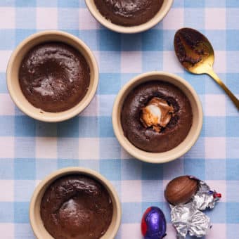 A table is set with four ramekins filled with Pinch of Nom's slimming-friendly Easter Creme Egg Lava Cakes; the gooey creme egg centre is oozing from one of the puddings.