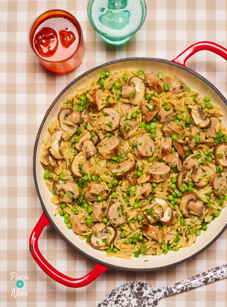 A large ovenproof casserole dish is filled with Pinch of Nom's slimming-friendly Herby Sausage Orzo,. A large serving spoon is beginning to scoop out a portion, ready to start dishing out.