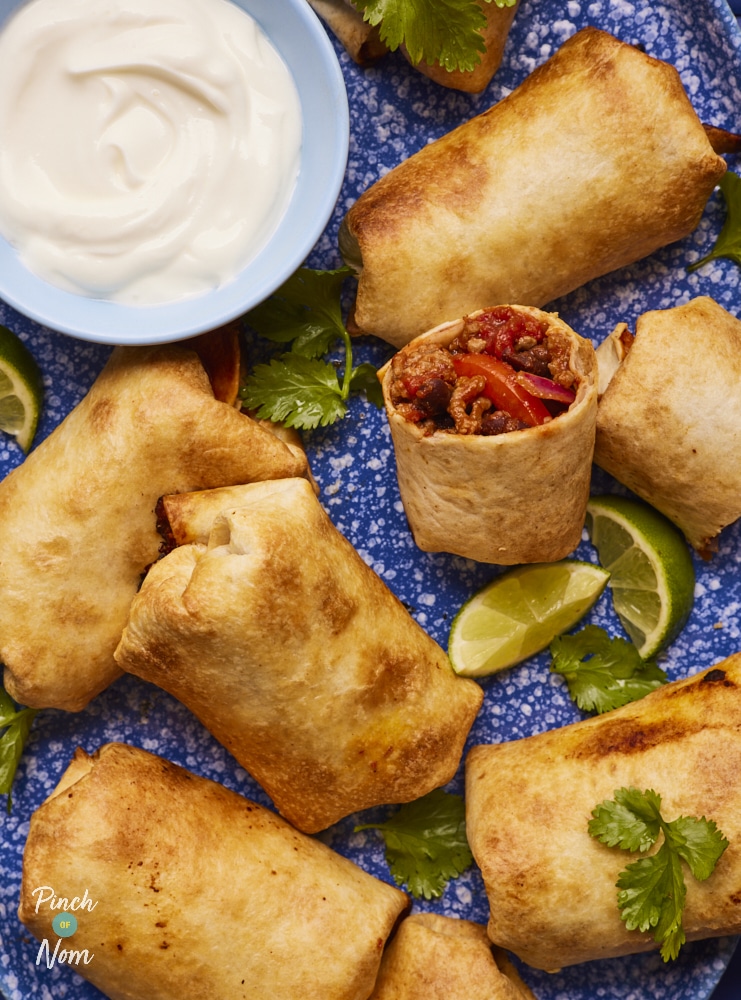 Pinch of Nom Baked BBQ Burritos, served on a plate with a creamy, cooling dressing and zingy slices of lime.